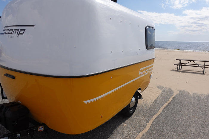 Experience the beach with an RV rental! A yellow and white Scamp camper parked beside the ocean on a sandy shore.