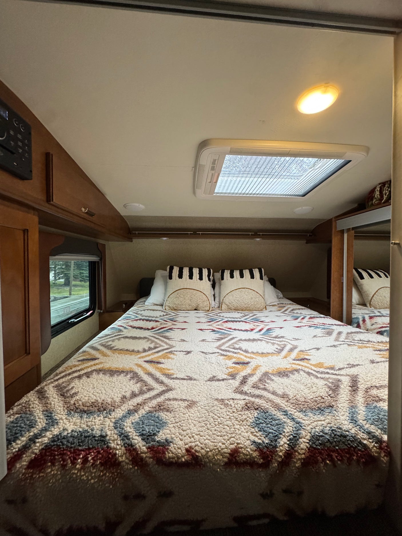 Cozy RV rental bedroom interior with patterned blanket, skylight, and window view.