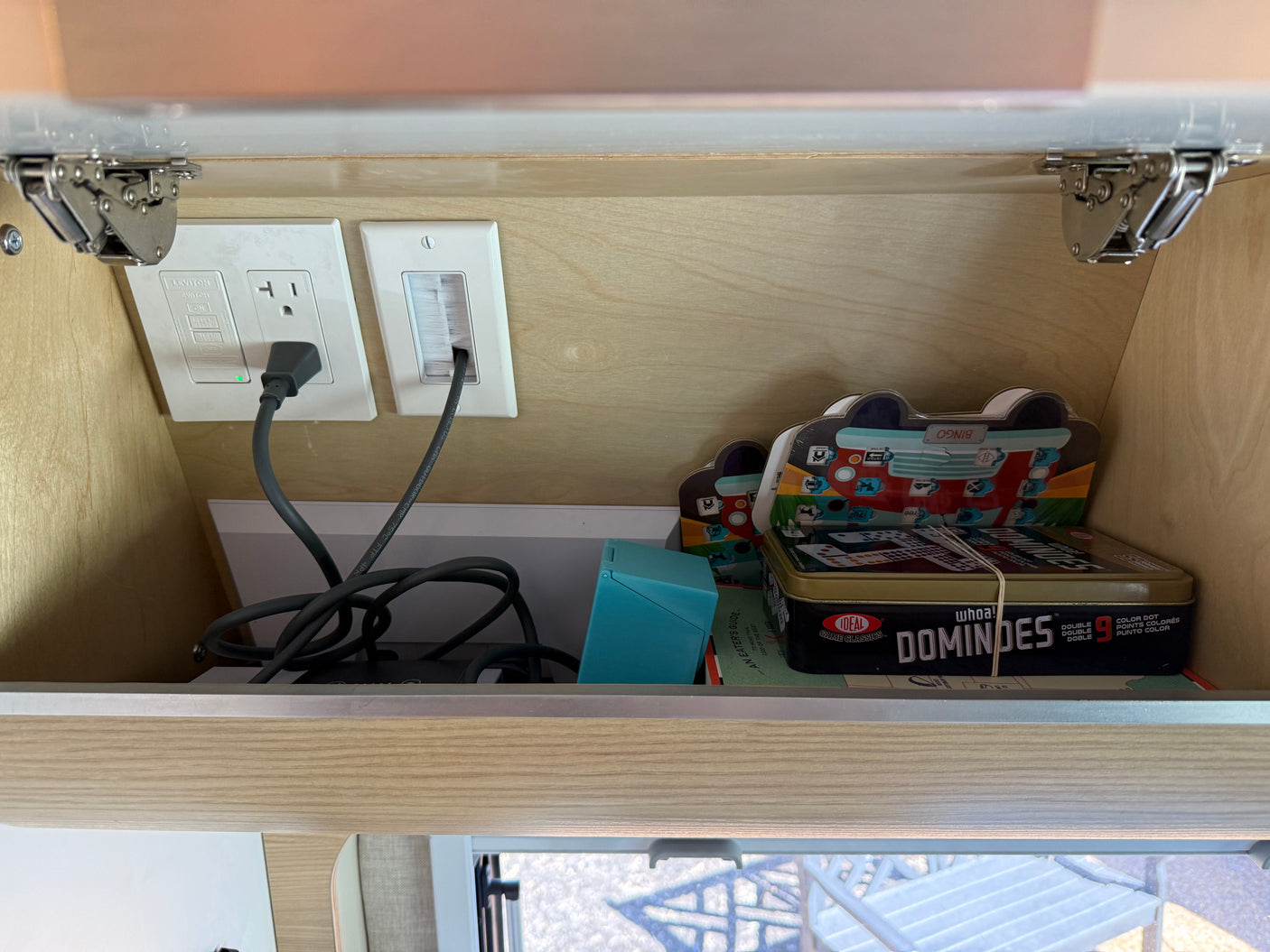 Inside an RV rental overhead cabinet: electrical outlets, cables, and travel games like Dominoes for entertainment on the go.