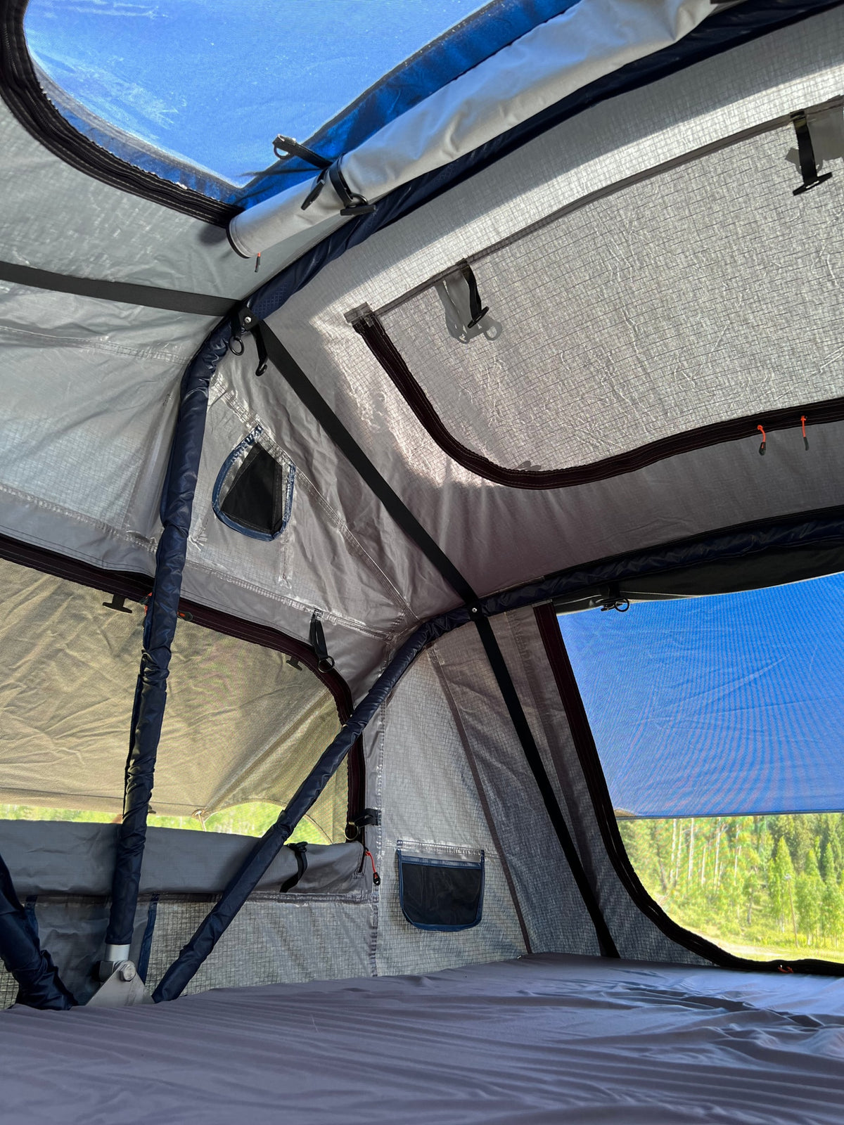 Explore nature with an RV rental! Interior view of a cozy rooftop tent with a mattress, mesh windows, and blue sky. — photo 16