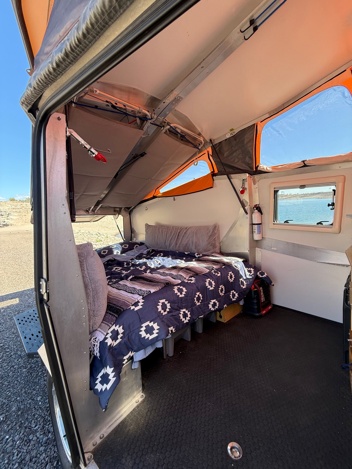 Cozy rv rental camper interior, featuring a patterned bed, lake view window, and open pop-top roof design.