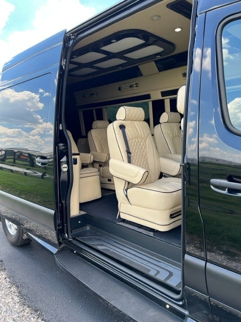 Step into luxury with this RV rental. A black van's open side door reveals a plush tan leather custom interior with captain's chairs.