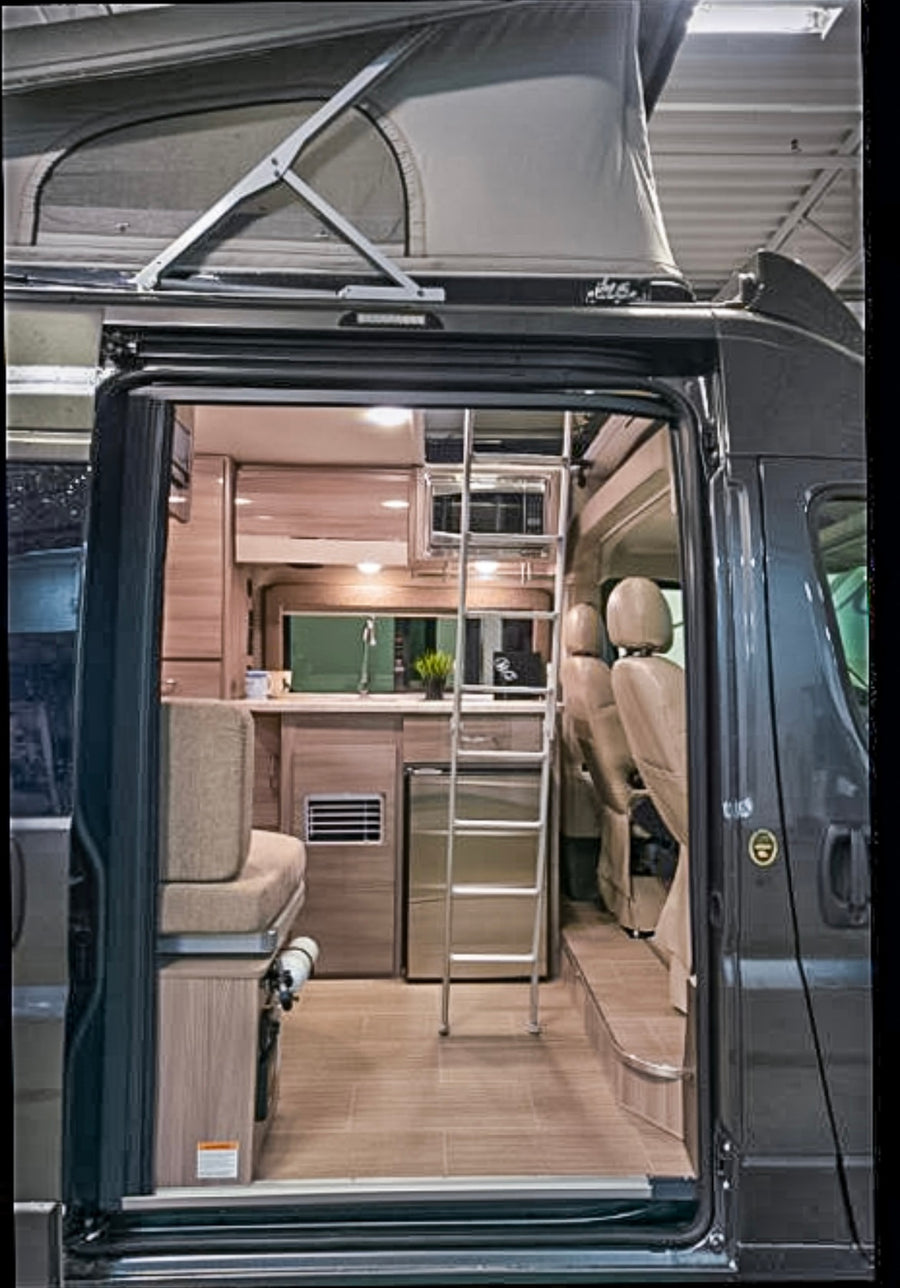 Explore this modern camper van RV rental interior! Features include a pop-top roof, kitchen, and ladder to an upper bed.