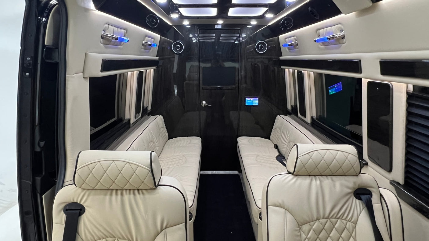 Luxury RV rental interior. View from front seats to the back, showing plush cream seating, dark glossy walls, and ambient blue lighting.