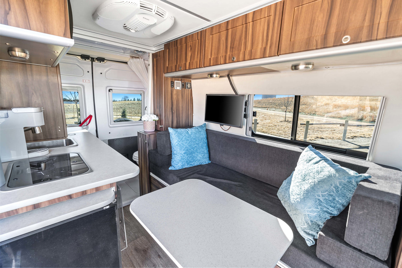 Inside a modern rv rental: bright interior with kitchen, comfy sofa, dining table, TV, and overhead storage.