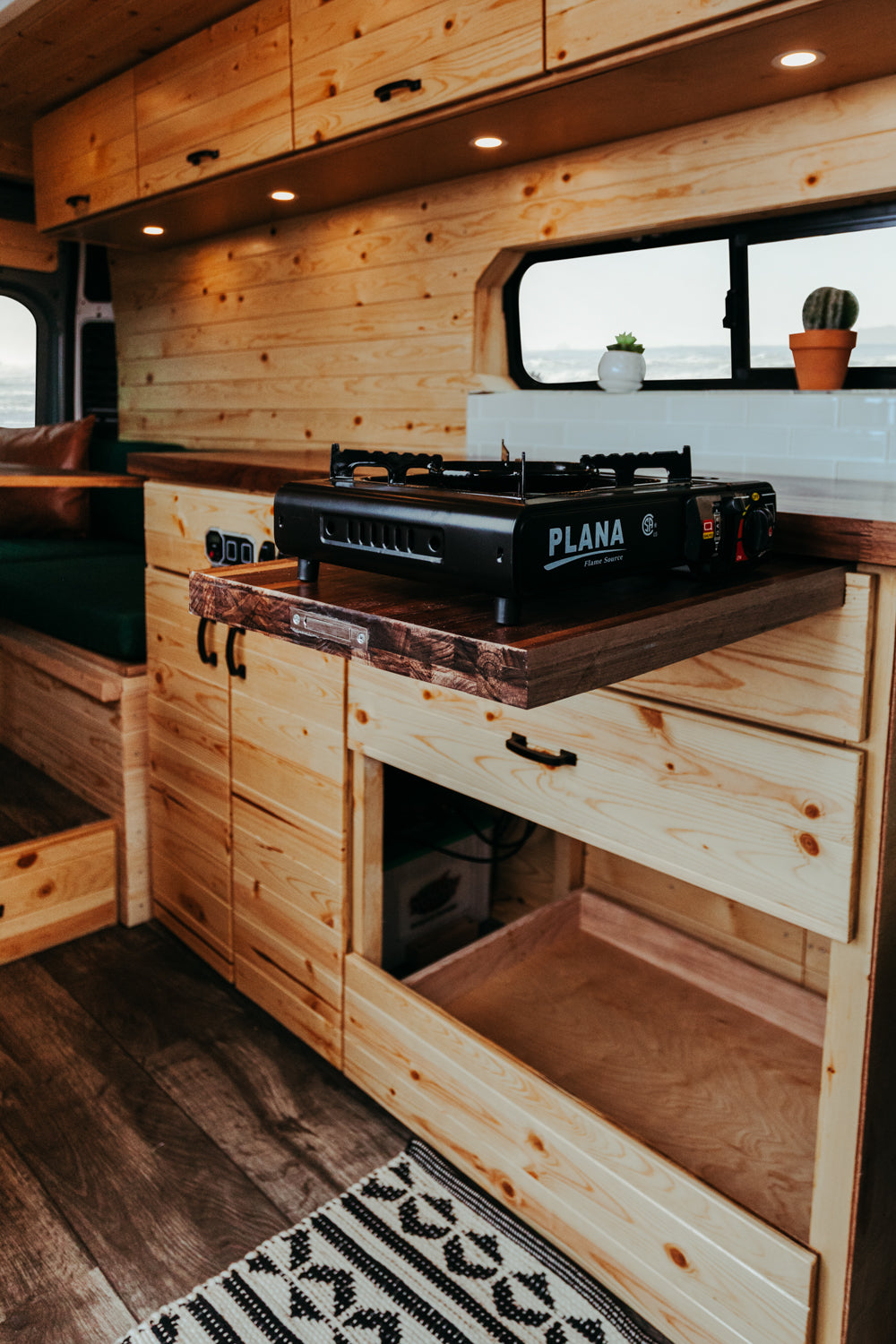 Cozy RV rental interior: wood-paneled walls, pull-out kitchen stove, custom cabinetry & storage.