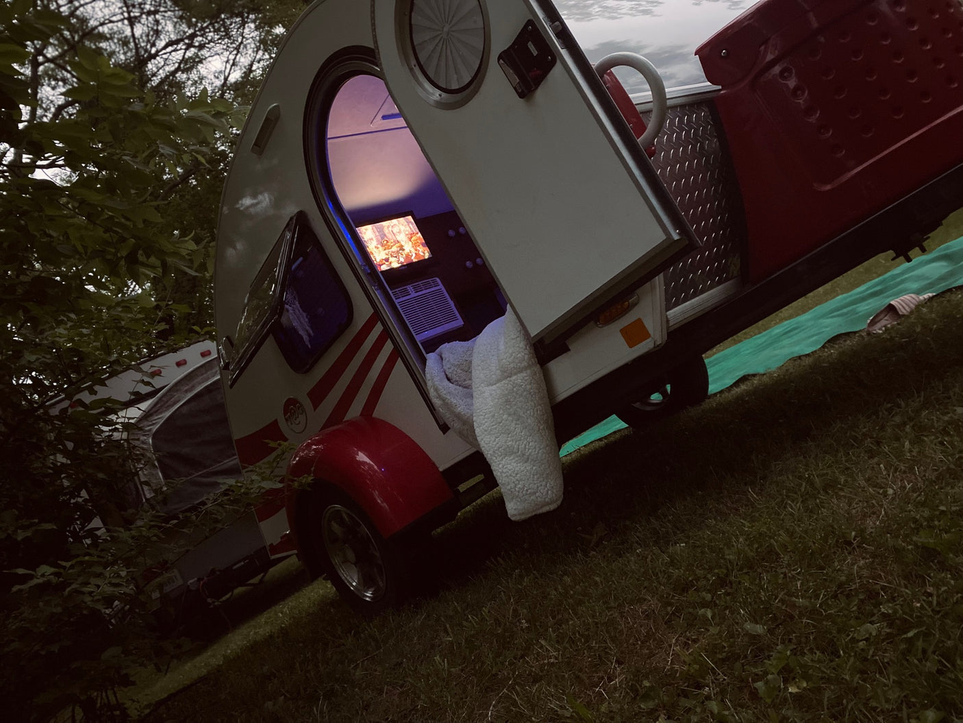 Comfortable RV rental at night: an open door reveals a lit interior with a screen, AC, and cozy blanket for camping.