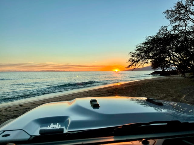 Golden sunset on a beach, viewed from a parked Jeep. Perfect RV rental travel adventure!