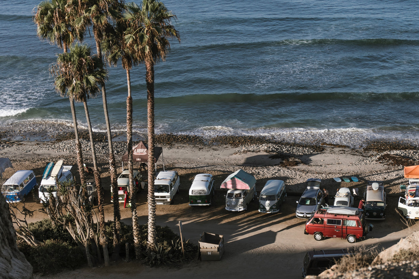 Vintage camper vans parked under palm trees on a sunny beach by the ocean. Perfect for an RV rental adventure!