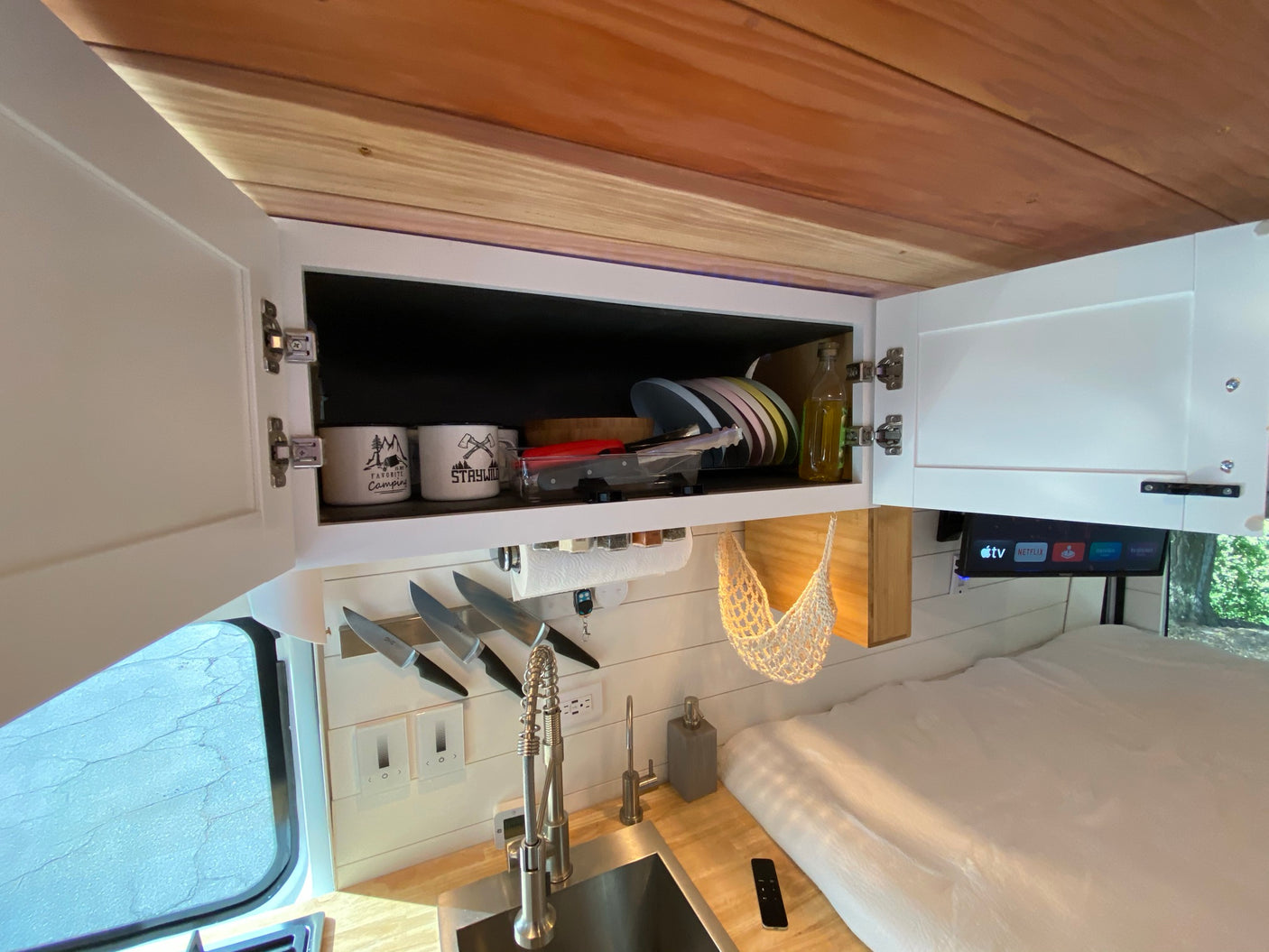 An RV rental's clever interior: compact kitchen with overhead storage, sink, and adjacent bed setup.