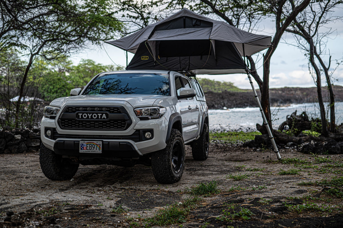 White Toyota Tacoma with a gray rooftop tent set up for coastal camping on Hawaii's lava rocks. Your adventure RV rental. — photo 5
