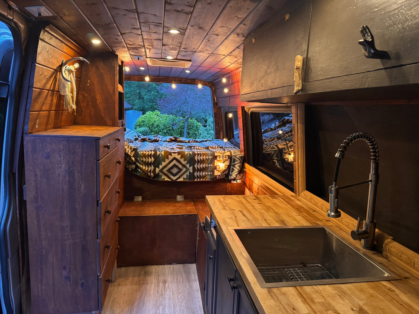 Step inside this charming RV rental: a rustic wooden camper van conversion featuring a bed, kitchen, and ambient lighting.