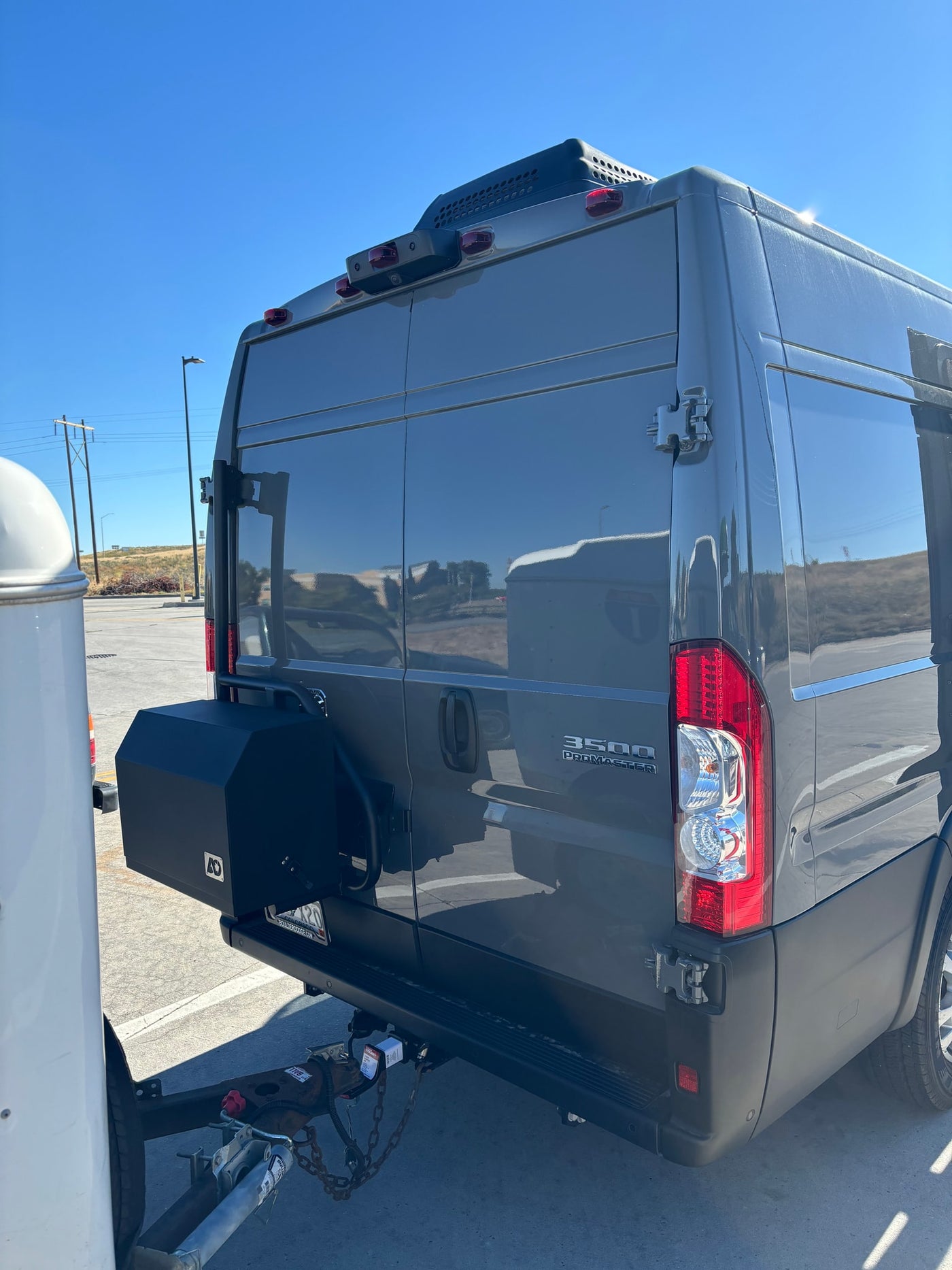 Rear view of a grey Ram ProMaster 3500 camper van, possibly an RV rental, with a tow hitch and storage box. — photo 20