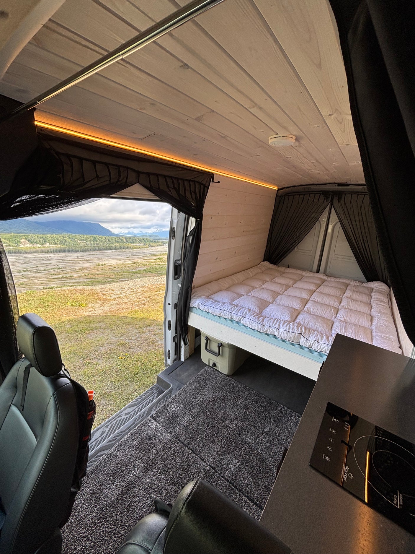 Inside an RV rental: a modern camper van conversion with a cozy bed, kitchen, and scenic mountain views.