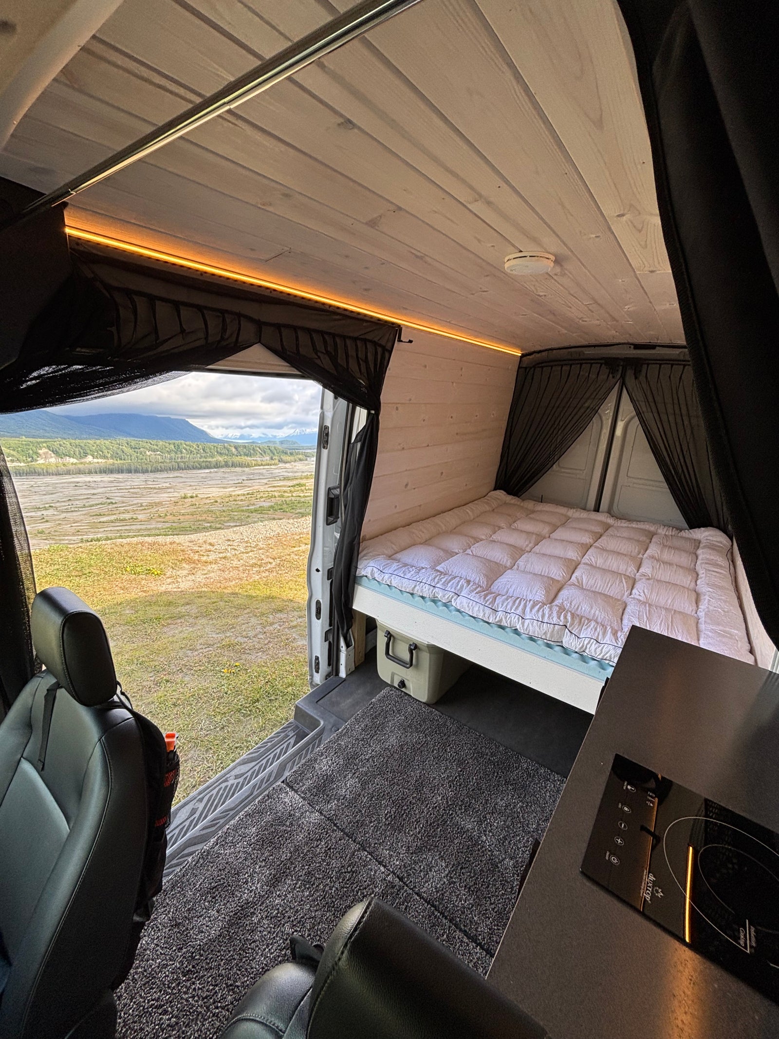 Inside an RV rental: a modern camper van conversion with a cozy bed, kitchen, and scenic mountain views.