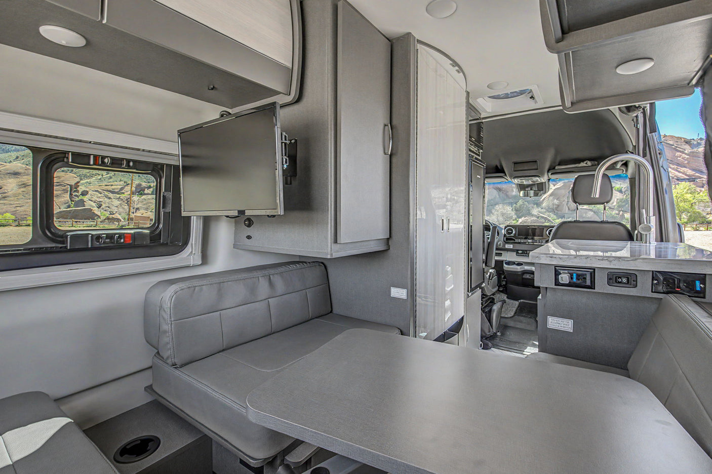 Inside a sleek rv rental: dinette, kitchen sink, TV, and scenic window view, ready for your next adventure.