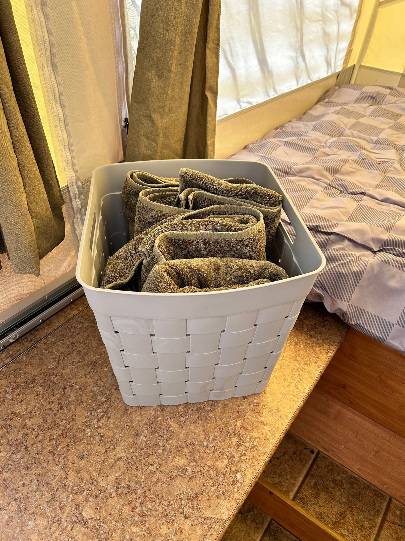 RV rental interior: A white basket with rolled towels sits on a counter beside a comfy bed with patterned bedding.