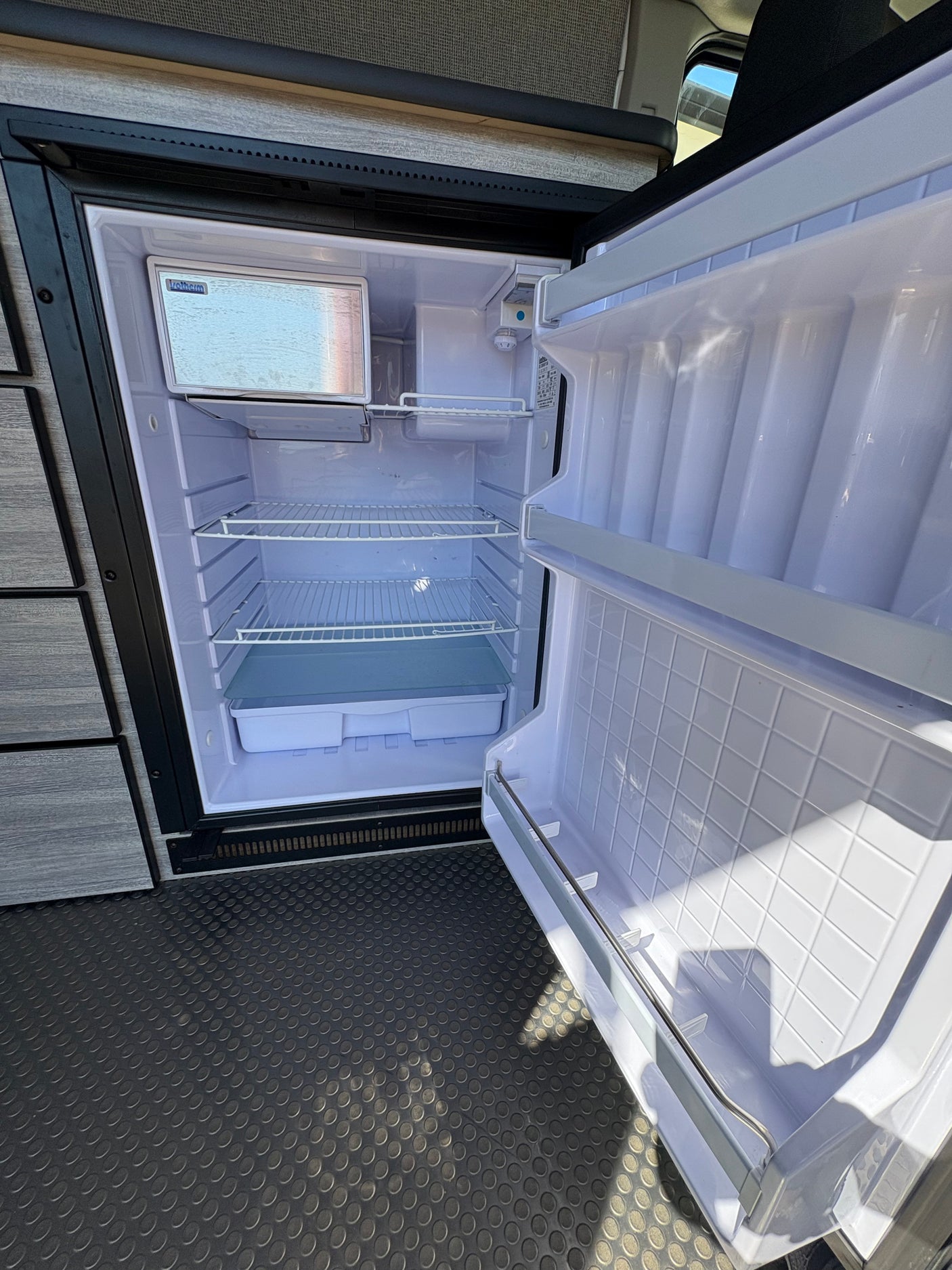 New RV rental fridge, spotless and ready for groceries, features freezer and adjustable shelves.