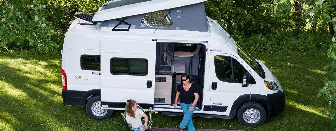 ready for your next RV rental adventure.|Two women relax by a white camper van RV rental with an extended pop-top roof — photo 2