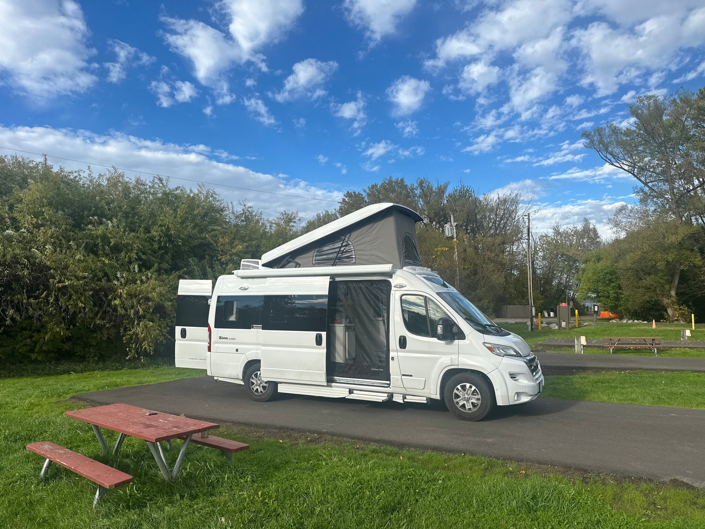 White pop-top rv rental camper van with open doors at a sunny campsite. A red picnic table is in the foreground.|Spacious rv rental interior: kitchen with microwave