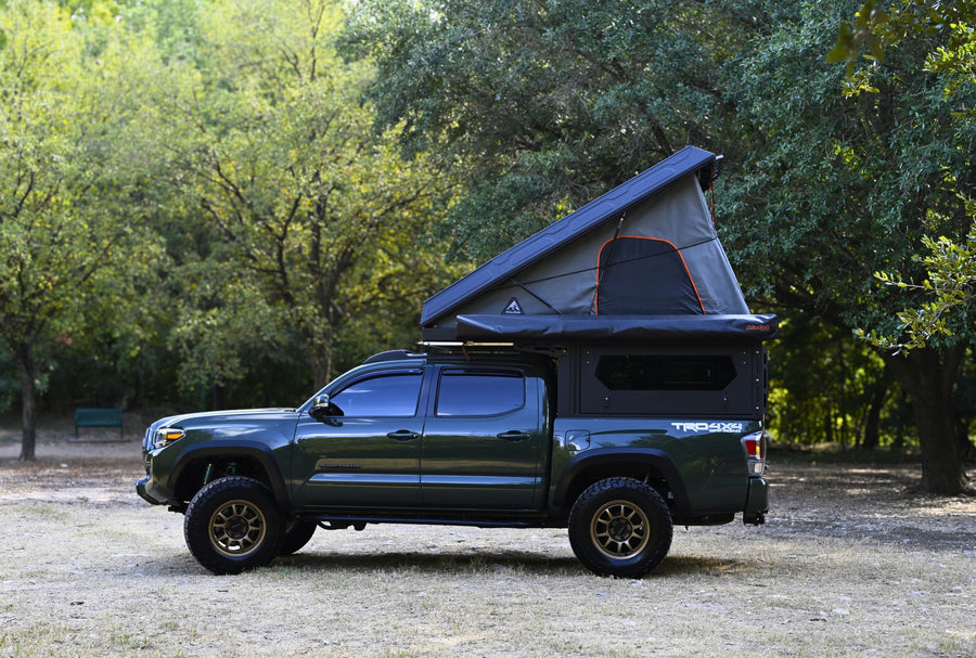This custom dark green Toyota Tacoma with a pop-up rooftop tent is an ideal RV rental for off-road adventures.