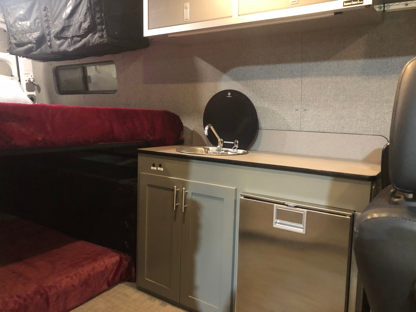 Experience comfort in this RV rental: compact kitchen with sink and fridge, plus a bed and overhead storage.