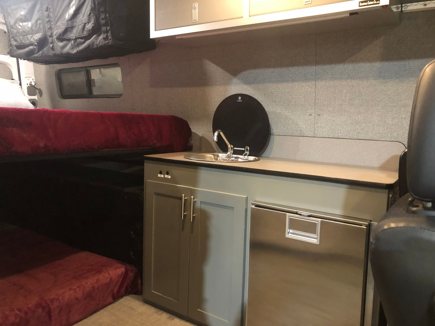 Experience comfort in this RV rental: compact kitchen with sink and fridge, plus a bed and overhead storage. — photo 7