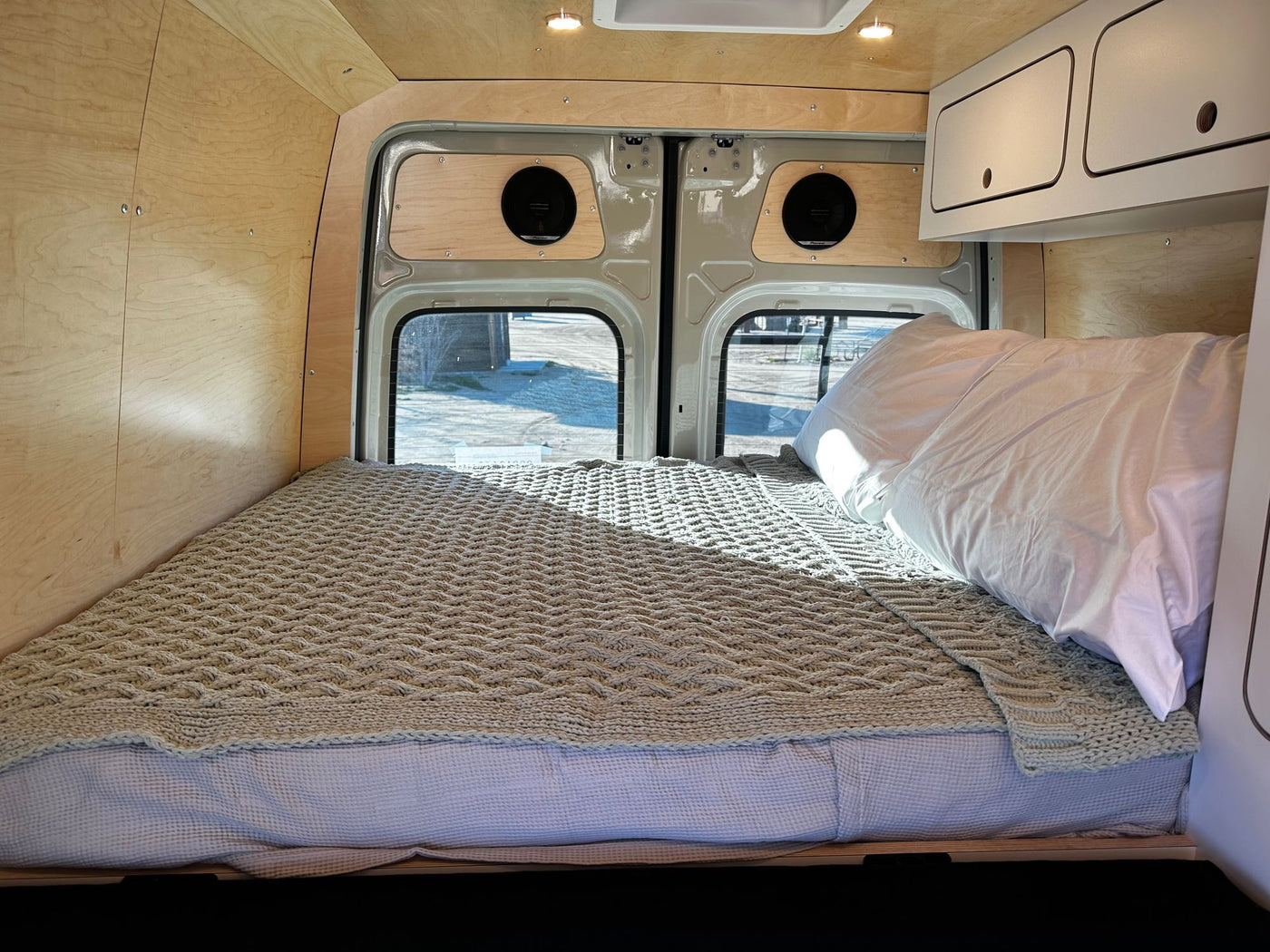 with Joshua trees.|Open rear doors of this RV rental reveal a functional camper van interior with raised bed — photo 3