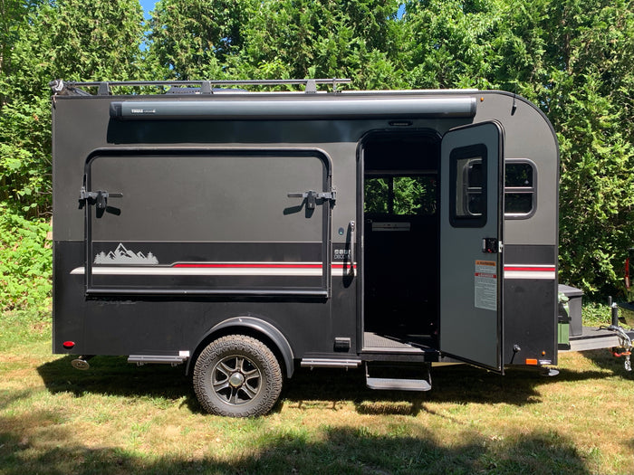 Dark grey InTech teardrop camper trailer with an open door, Thule awning, and rugged tires, great for an RV rental.
