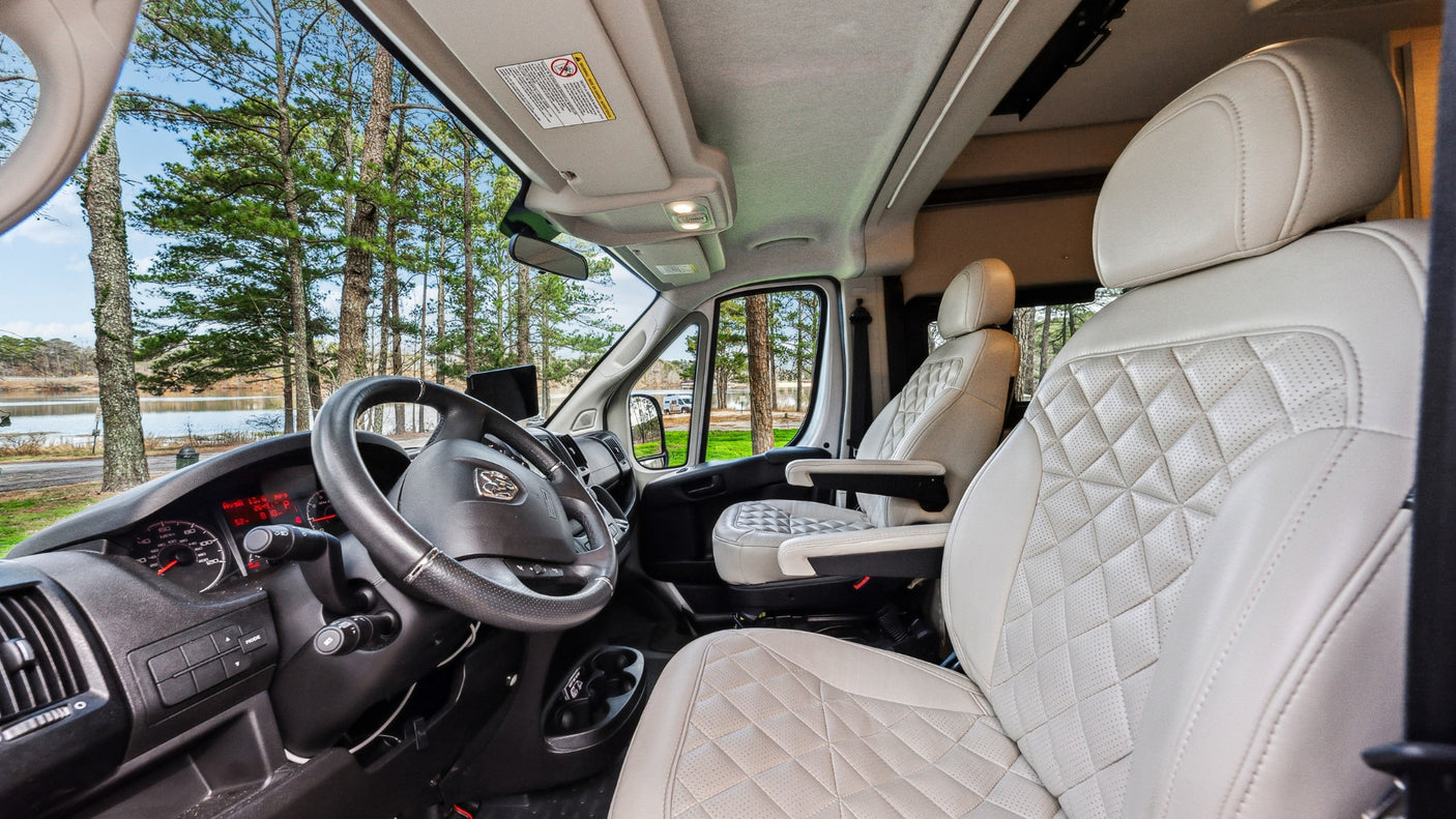 RV rental's front cabin featuring white quilted seats, detailed dashboard, and a picturesque lake view.