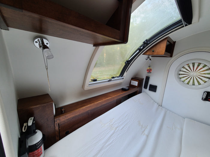 Cozy RV rental interior: a compact bedroom features a bed, wooden storage, a large window, and essential controls.