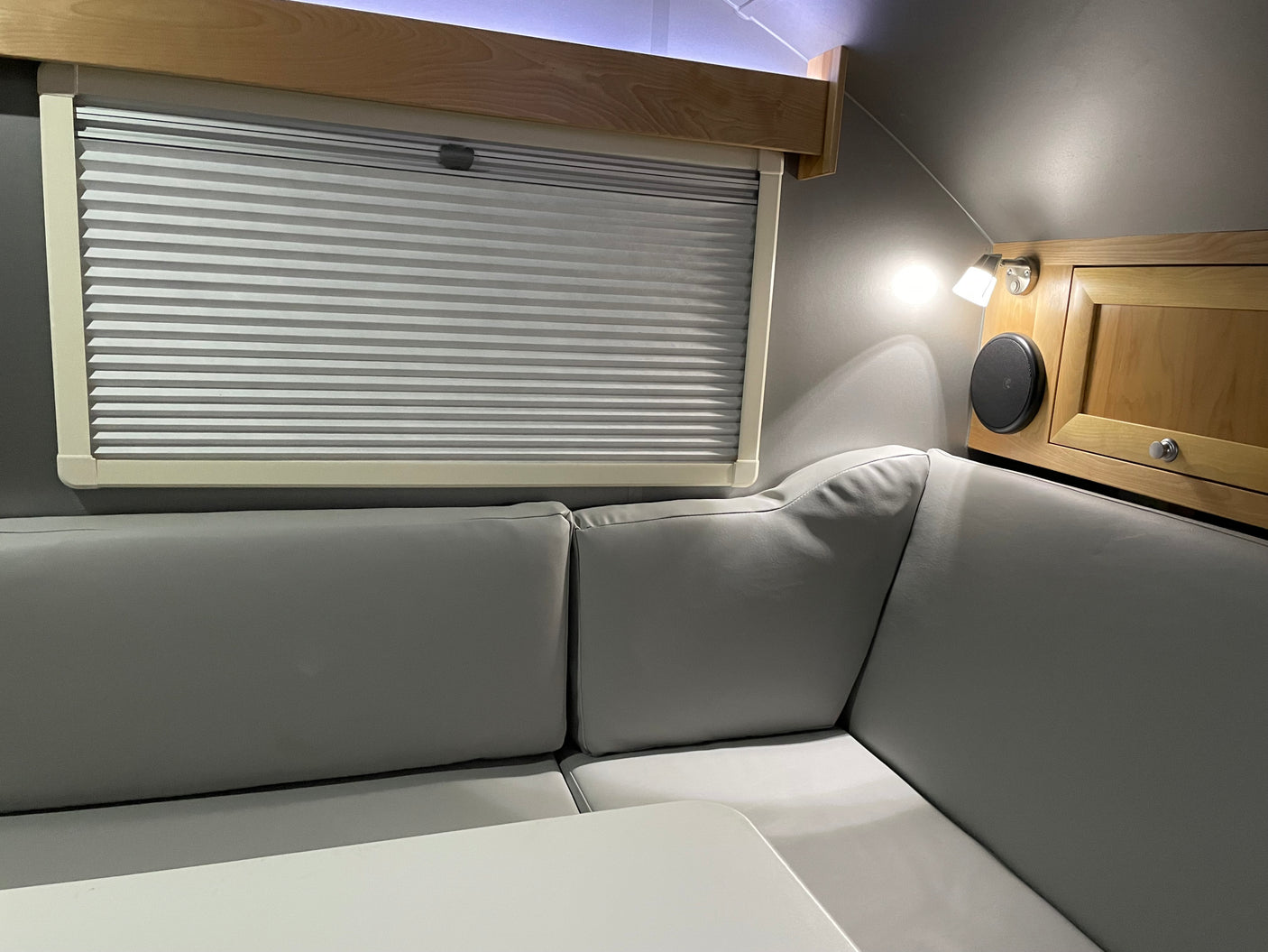 Cozy RV rental interior featuring light gray dinette seating, a table, pleated window blind, and wood cabinetry.