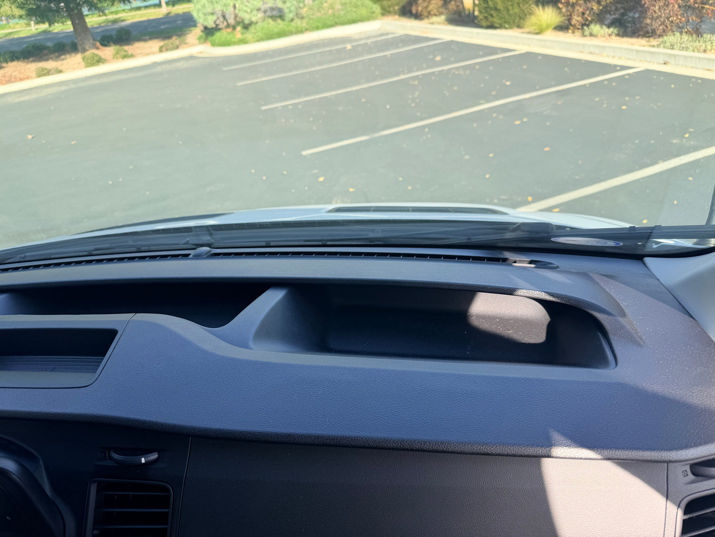 RV rental dash & windshield view, facing a sunny parking lot. Dashboard compartment, vents, and windshield sticker visible.