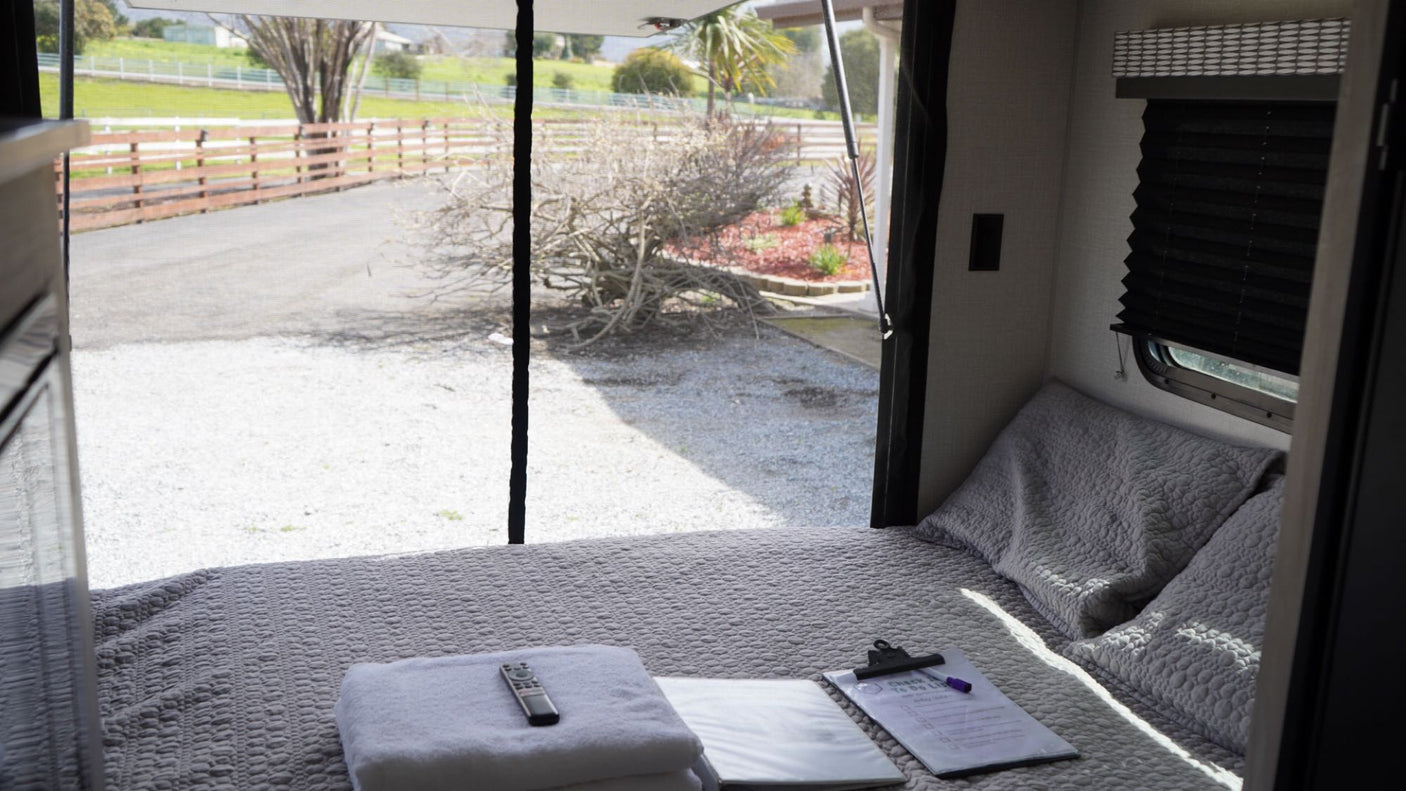Cozy RV rental bedroom with a comfortable bed, fresh towels, and a tranquil view of the fenced outdoors.
