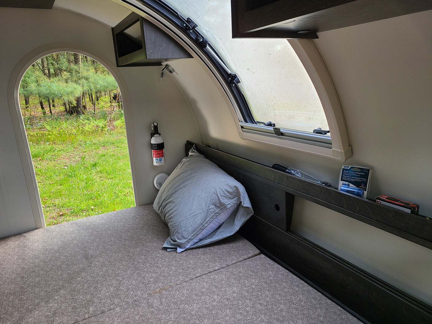 RV rental interior: bed, window, safety gear, and an open archway to a vibrant green forest view.