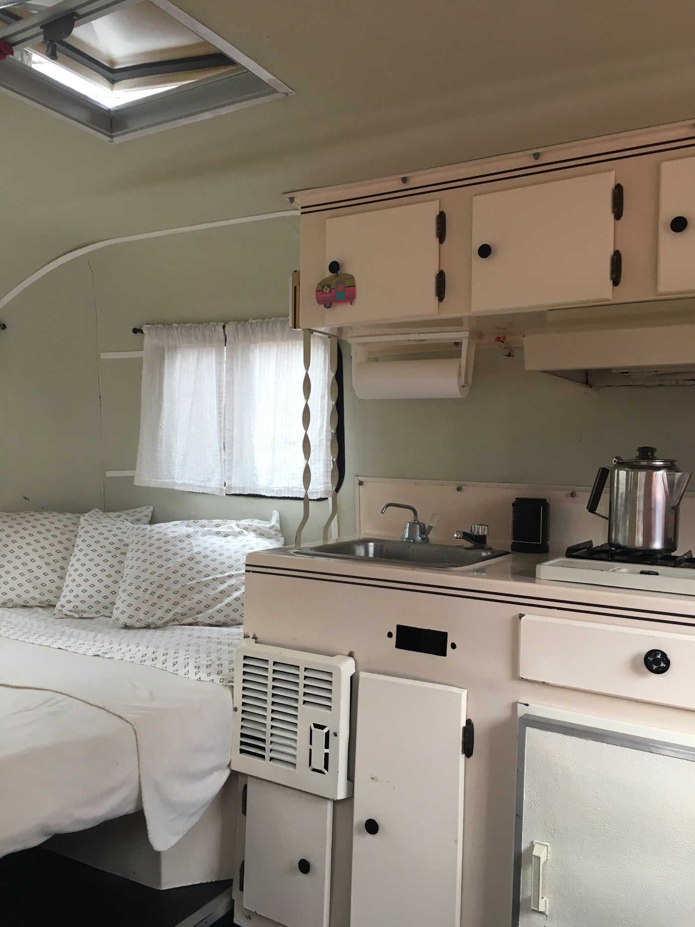 Cozy RV rental interior with bed, compact kitchen, overhead cabinets, and a ceiling vent. — photo 7