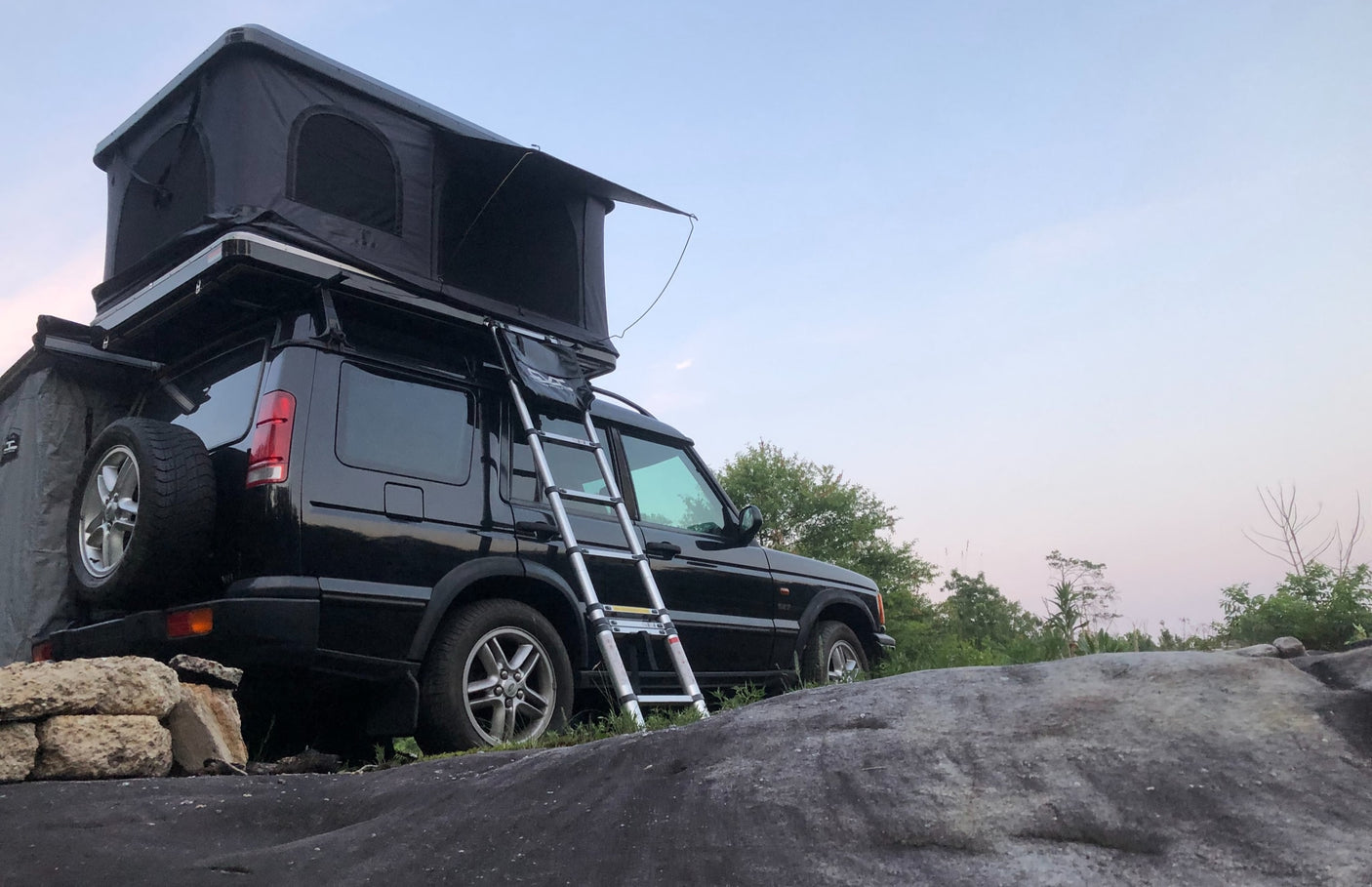 A black Land Rover SUV with a deployed roof-top tent and ladder