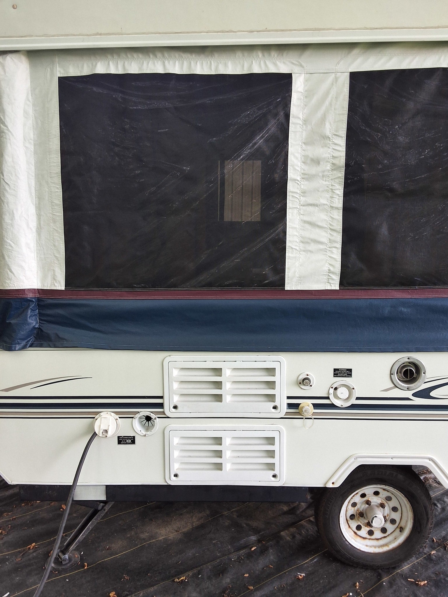 Ready for your RV rental: side view of a pop-up camper with canvas tent, utility hookups, and tire visible.