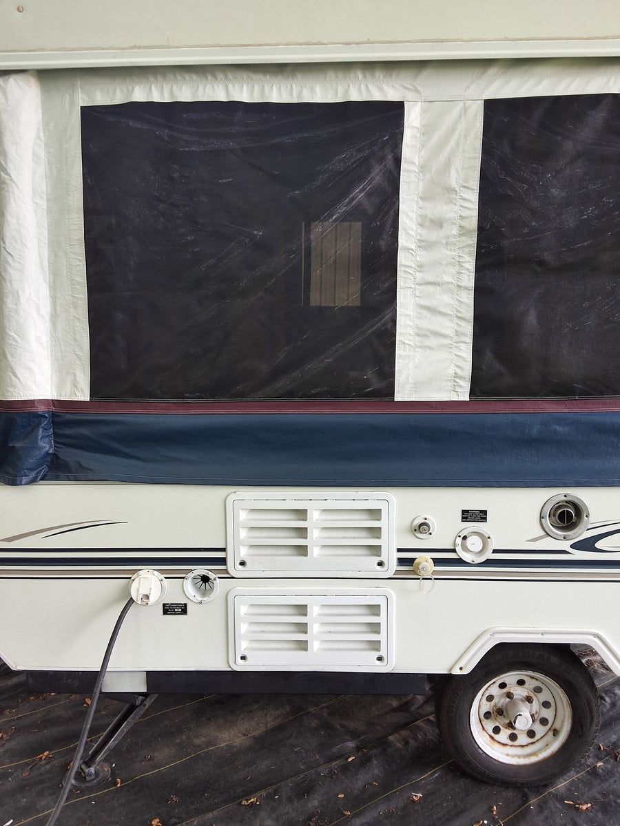 Ready for your RV rental: side view of a pop-up camper with canvas tent, utility hookups, and tire visible.