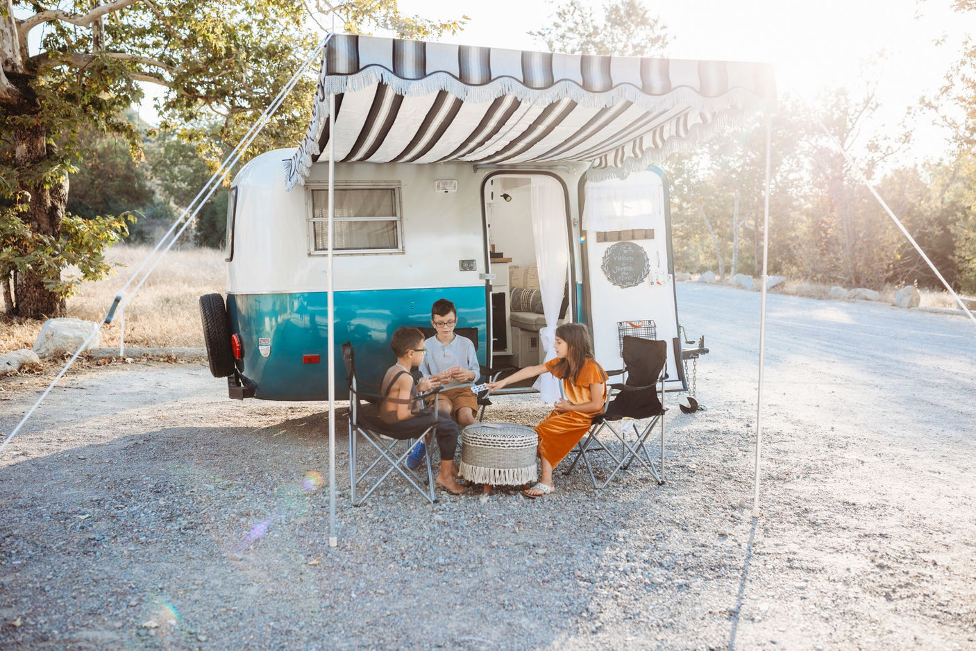 Three kids enjoy a family camping trip, playing cards outside their charming vintage RV rental with an extended awning.