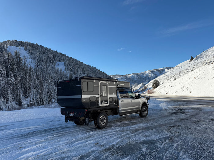 Rugged Four Wheel Campers Hawk+ truck camper on icy winter roads, surrounded by snowy mountains. Perfect for an rv rental adventure.