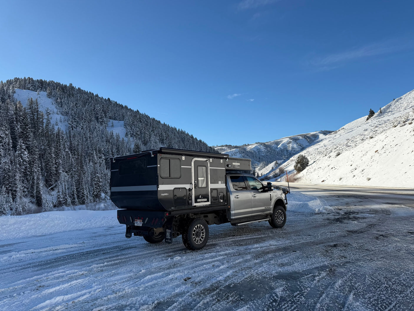 Rugged Four Wheel Campers Hawk+ truck camper on icy winter roads, surrounded by snowy mountains. Perfect for an rv rental adventure.