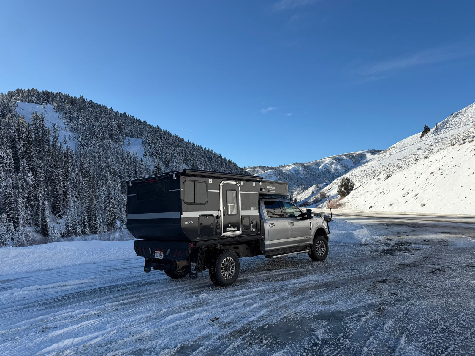 Rugged Four Wheel Campers Hawk+ truck camper on icy winter roads, surrounded by snowy mountains. Perfect for an rv rental adventure.