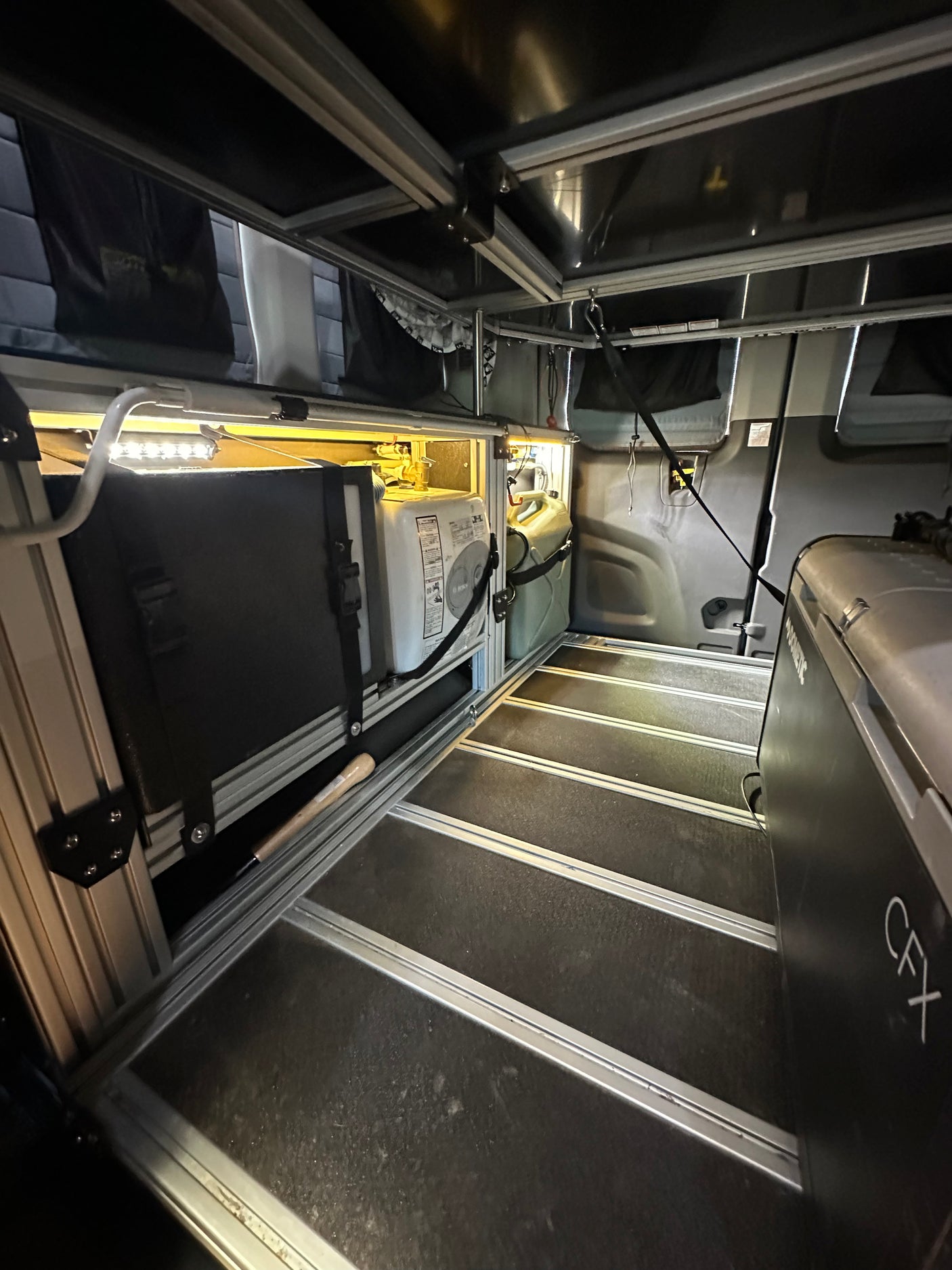 RV rental interior shows a Dometic fridge, water heater, and water jug in a modular camper van setup with LED lighting.