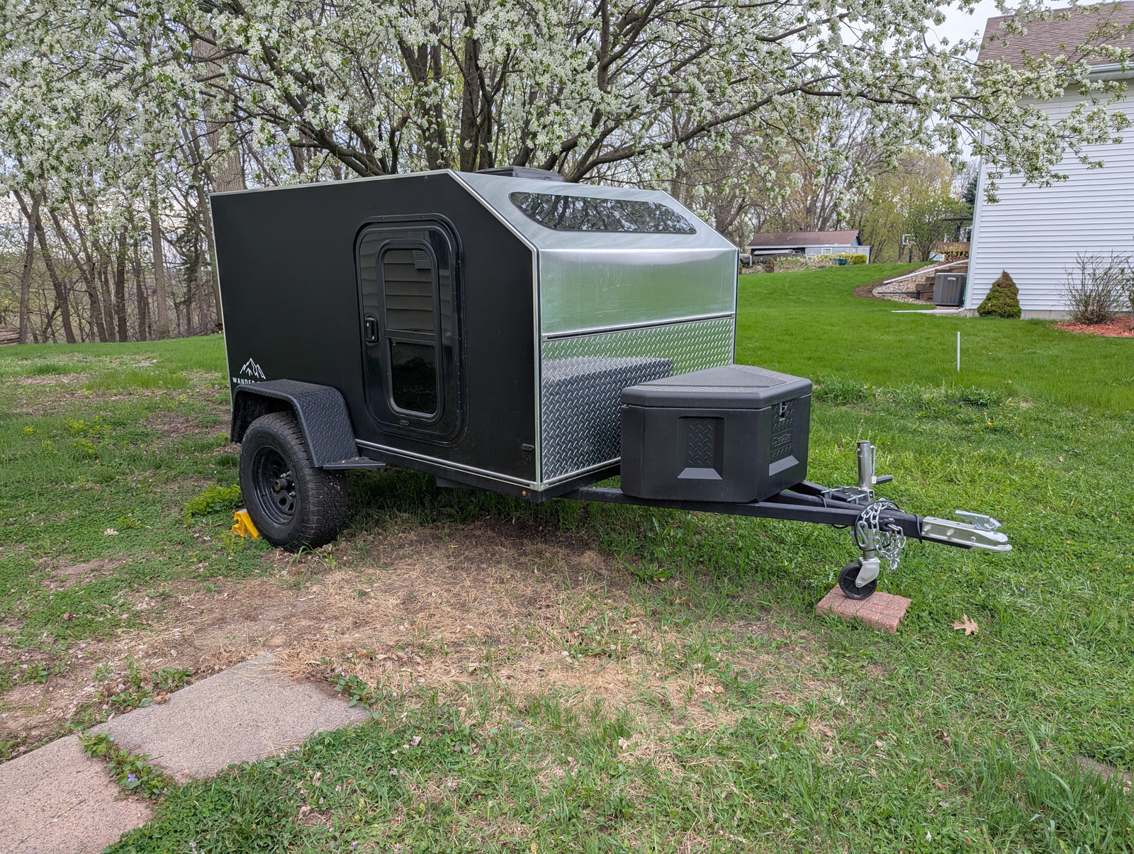 Explore with this black & silver teardrop camper rv rental, parked under a flowering tree.