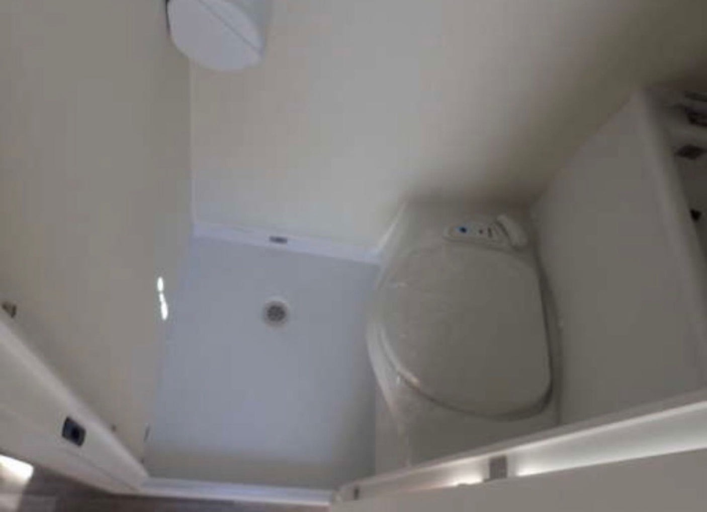 An RV rental's compact bathroom, showing a white toilet and a separate shower area with a floor drain.
