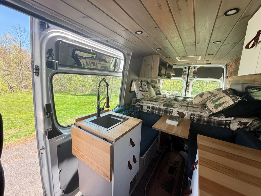 Inviting camper van interior with a kitchen, cozy bed, and scenic outdoor views, ideal for your next RV rental.