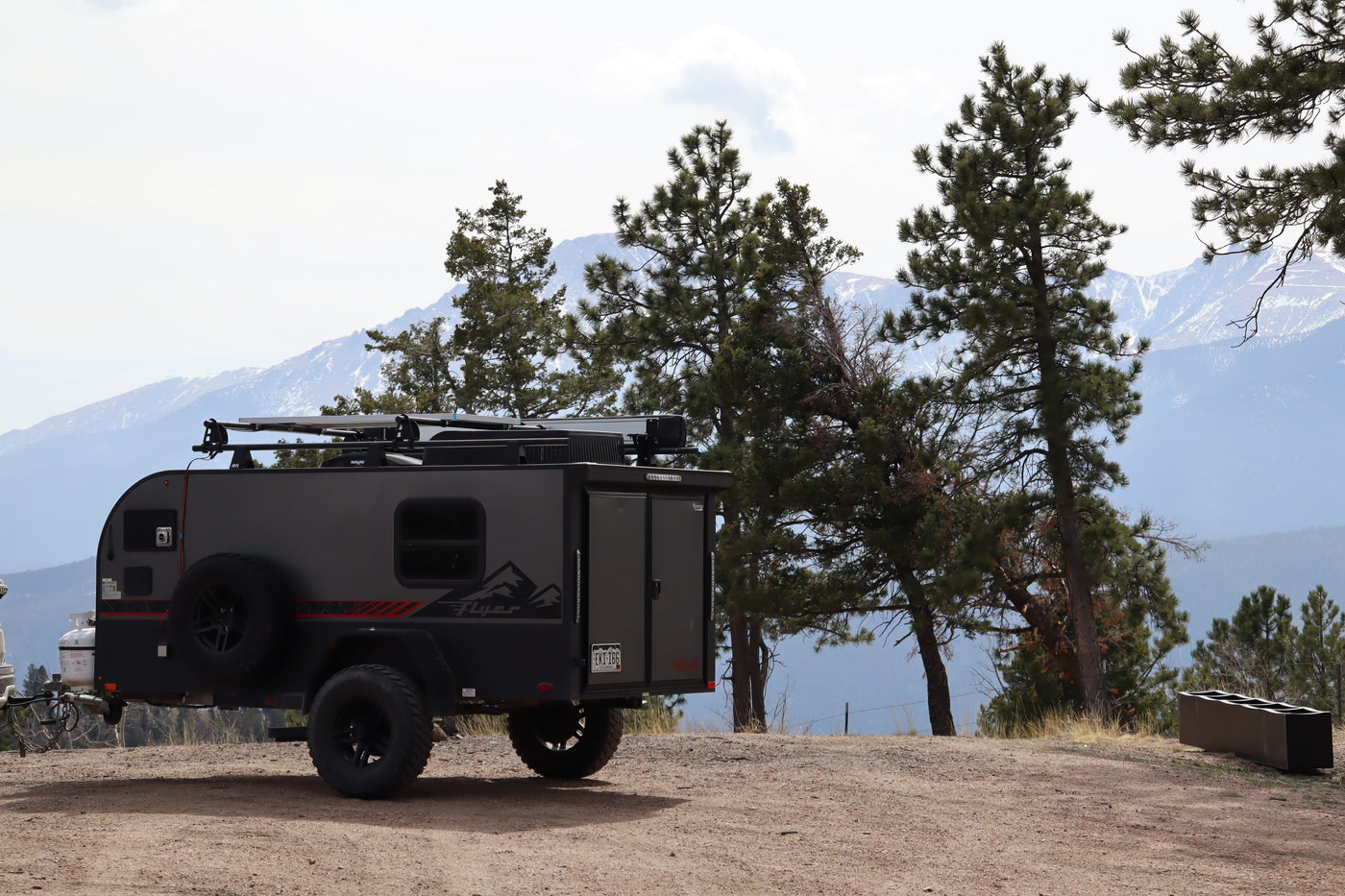 Rugged teardrop RV rental parked on a dirt road, ready for adventure amidst pine trees and snowy mountains. — photo 11