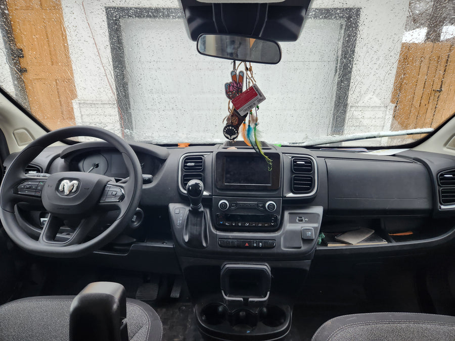 Inside a modern rv rental van: rainy windshield view, Ram dashboard with steering wheel, infotainment, and gear shift.