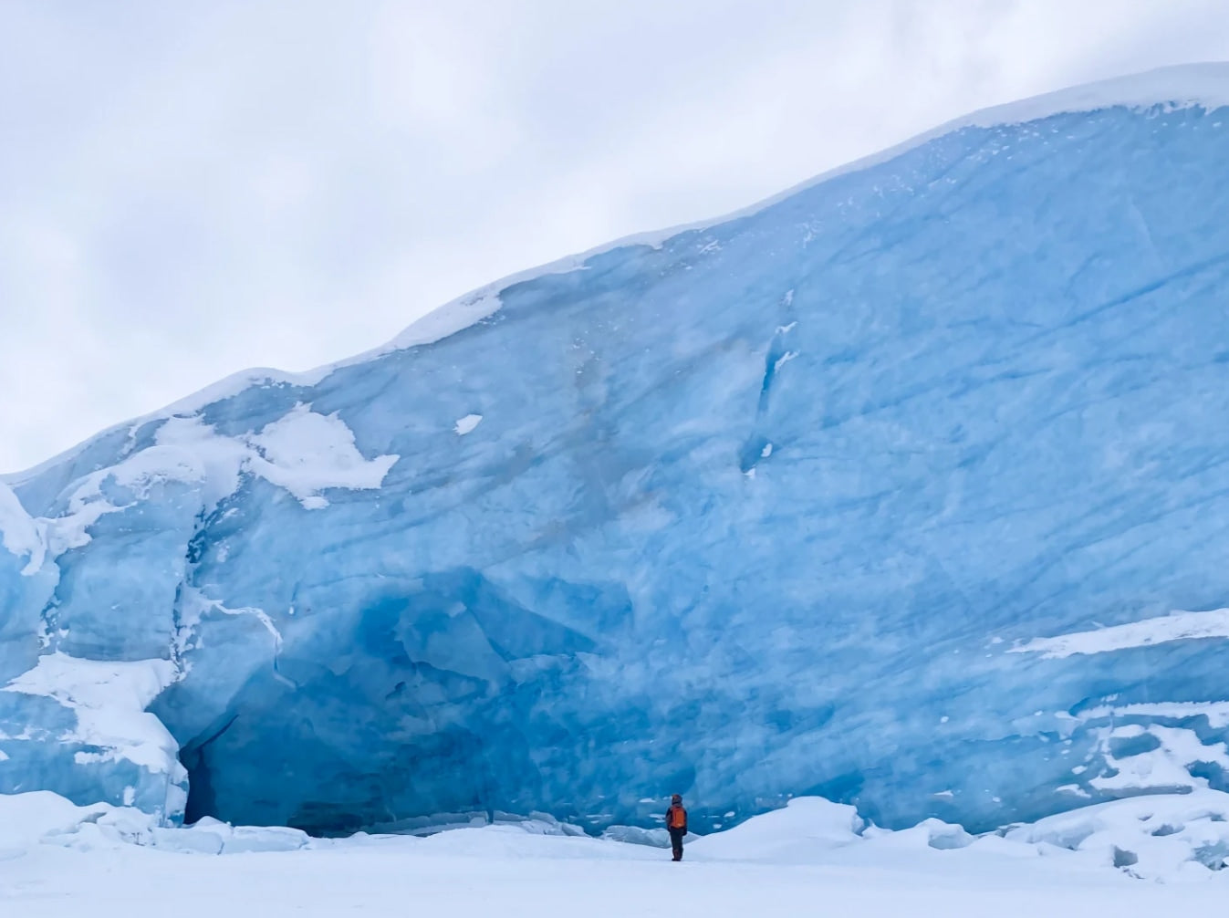 An adventurer stands before a colossal blue glacier, surrounded by snow. Experience such grandeur with an RV rental!